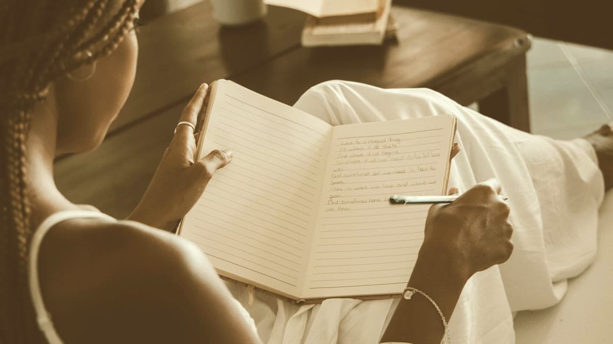 Alguien escribe a mano en un diario abierto, sentado junto a una ventana