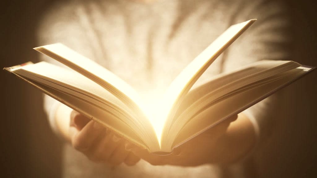 Unas manos sostienen un libro abierto del que sale una luz cálida